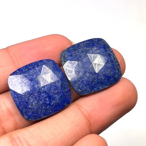 Könnte beinhalten: Zwei quadratische, facettierte Lapislazuli-Edelsteine in tiefem Blau mit silbernen Flecken.