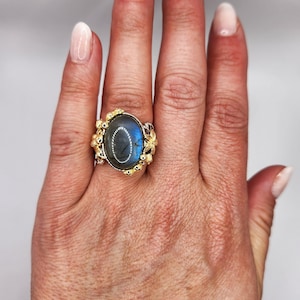 May include: A silver ring with a large oval blue labradorite gemstone set in a gold floral design.