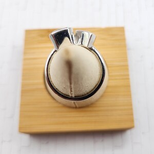 May include: A silver ring with two clear gemstones set in a prong setting. The ring is displayed on a wooden ring holder.