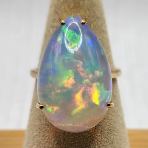 May include: A pearlescent teardrop-shaped opal ring set in yellow gold. The opal displays a rainbow of colours, including green, blue, orange, and yellow.