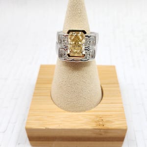 May include: A two-piece ring set with a large, yellow, cushion-cut diamond surrounded by smaller diamonds. The ring is set in white gold with a yellow gold band.