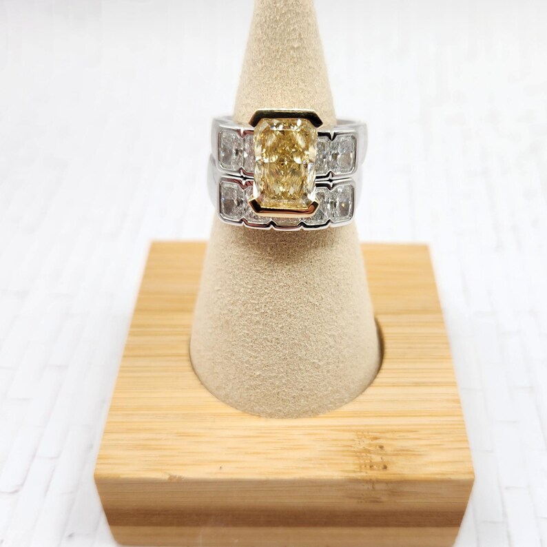 May include: A two-piece ring set with a large, yellow, cushion-cut diamond surrounded by smaller diamonds. The ring is set in white gold with a yellow gold band.