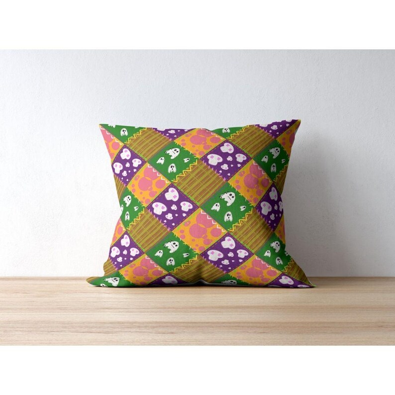 Close-up mockup of a single throw pillow showcasing the repeating patchwork ghost and skull seamless pattern on fabric.