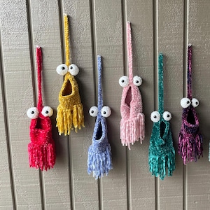 May include: Seven crocheted hanging ornaments with googly eyes and fringe. The ornaments are in various colors, including red, yellow, pink, blue, and green.