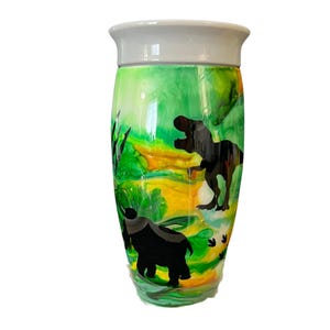 May include: A green and yellow tumbler with a white lid. The tumbler has a silhouette of a dinosaur and other prehistoric creatures.
