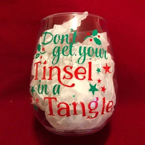 Pode incluir: Uma ta&ccedil;a de vinho de vidro transparente com um decalque de vinil vermelho e verde que diz "Don't get your Tinsel in a Tangle".
