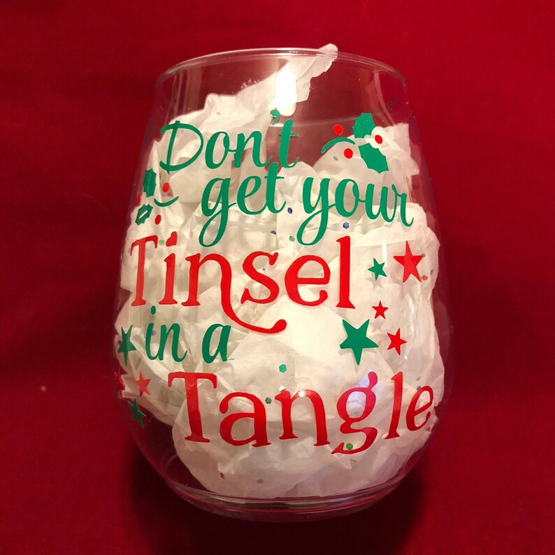 Pode incluir: Uma ta&ccedil;a de vinho de vidro transparente com um decalque de vinil vermelho e verde que diz "Don't get your Tinsel in a Tangle".