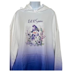 May include: White hooded sweatshirt with a purple ombre fade to blue. The sweatshirt has a purple snowman with a purple hat and scarf in a wreath of purple flowers and berries. The text "Let it Snow" is printed in purple above the snowman.