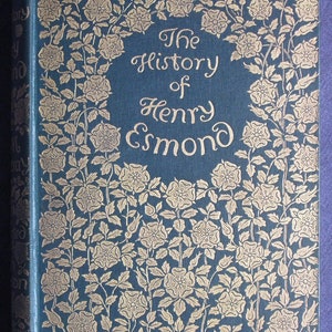 May include: A hardback book, "The History of Henry Esmond", with a blue cover and gold floral detailing. The title is in ornate script. The spine is also blue, with the title visible.