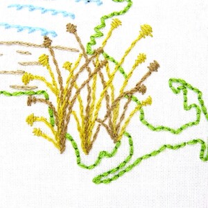 Puede incluir: Dise&ntilde;o bordado de una isla verde con un grupo de flores amarillas y marrones en el centro. El dise&ntilde;o est&aacute; cosido en tela blanca.