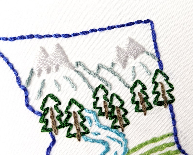 May include: Embroidered design of a mountain scene with blue, green, and white thread. The design features three mountains, trees, and a river.