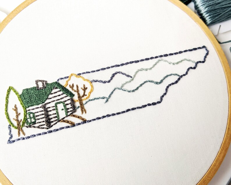 May include: Embroidered design of the state of Tennessee with a cabin, trees, and mountains in shades of green, brown, and blue.