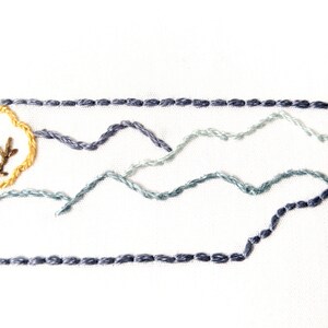May include: Embroidered design of a tree with a yellow sun behind it, and three rows of blue mountains in the background.