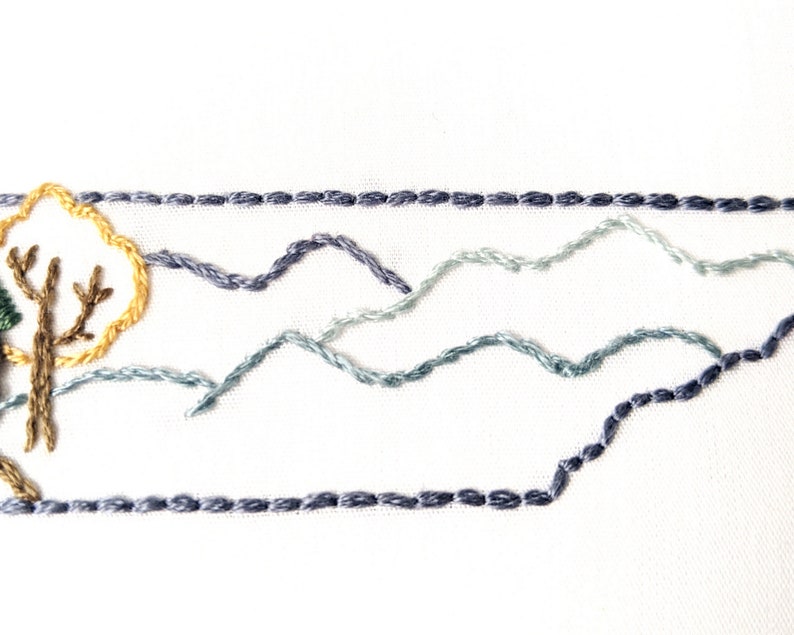 May include: Embroidered design of a tree with a yellow sun behind it, and three rows of blue mountains in the background.