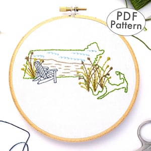 Könnte beinhalten: Ein gesticktes Design des Bundesstaates Massachusetts mit einer Strandszene, einschließlich eines Stuhls, Wellen und Gras. Das Design ist auf weißem Stoff in einem hölzernen Stickrahmen gestickt. Der Text "PDF Pattern" ist in der oberen rechten Ecke des Bildes sichtbar.