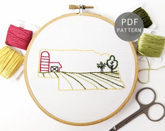 May include: Embroidered hoop art featuring a red barn with a silo, green trees, and yellow fields, representing a farm scene. The hoop is surrounded by embroidery floss in various colors, including red, yellow, and green.