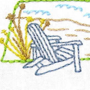 Puede incluir: Dise&ntilde;o bordado de una silla Adirondack azul en una playa con hierba amarilla y marr&oacute;n y olas azules en el fondo.