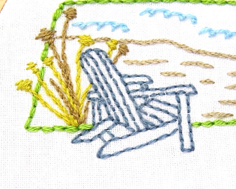 Puede incluir: Dise&ntilde;o bordado de una silla Adirondack azul en una playa con hierba amarilla y marr&oacute;n y olas azules en el fondo.
