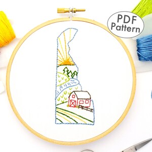 Könnte beinhalten: Ein PDF-Muster für ein Stickprojekt mit einem Stickrahmen, das eine stilisierte Umrandung des Bundesstaates Delaware mit einem roten Schuppen, grünen Bäumen, einem blauen Fluss und einer gelben Sonne zeigt.