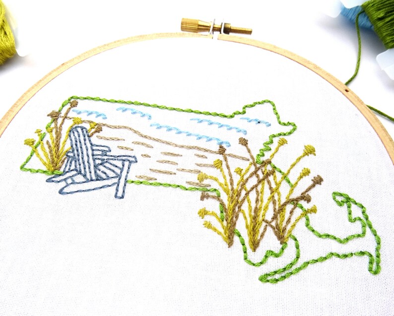 Puede incluir: Dise&ntilde;o bordado del estado de Massachusetts con una escena de playa, que incluye una silla Adirondack azul, arena marr&oacute;n, olas azules y juncos verdes y amarillos.