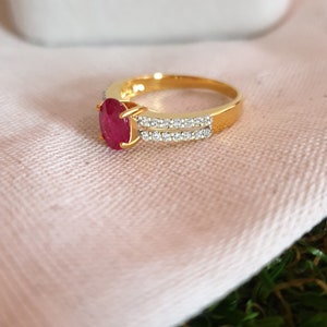 May include: A gold ring with a red oval gemstone and a double row of clear round gemstones.