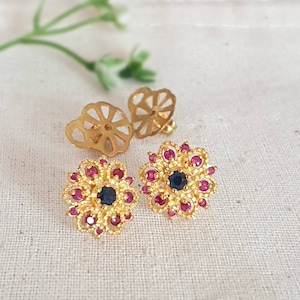 May include: A pair of gold earrings with a floral design. The earrings have a blue center stone and are surrounded by pink stones.