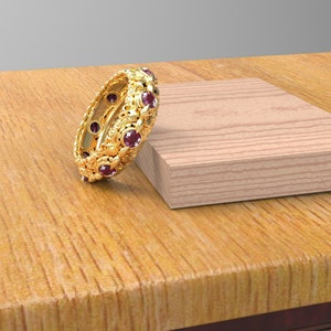Könnte beinhalten: Ein goldener Bandring mit einem dekorativen Design und roten Edelsteinen.