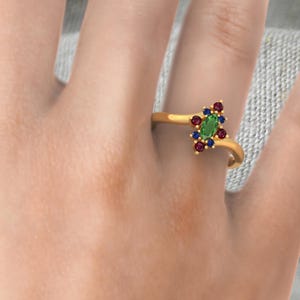 May include: A gold ring with a green oval gemstone surrounded by smaller red and blue gemstones.