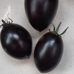 Puede incluir: Tres tomates de color morado oscuro con tallos verdes. Los tomates son redondos y lisos.