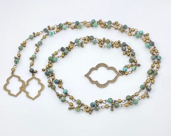 May include: A long, layered necklace with turquoise and gold beads. The necklace features a large, ornate pendant in the shape of a quatrefoil.