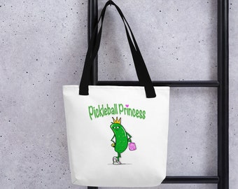 May include: White tote bag with black handles. The bag has a green pickle character wearing a gold crown and holding a pink purse. The text "Pickleball Princess" is written in green letters with a pink heart.