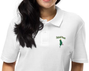 May include: White polo shirt with a green pickle wearing a crown and holding a pickleball. The text "Pickleball Princess" is above the pickle.