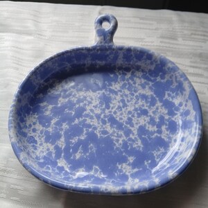May include: Blue and white speckled ceramic serving dish with a handle. The dish is oval-shaped and has a raised rim. The handle has a hole for hanging. The speckled pattern is white on a blue background.