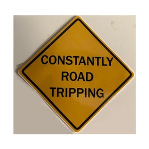 May include: A yellow diamond-shaped road sign with black text that reads "CONSTANTLY ROAD TRIPPING".