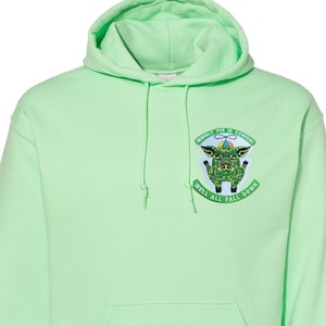 May include: A light green hoodie with a front pocket and drawstring hood. The hoodie features a graphic of a pig with text that reads "Whirly Pig is Coming" and "We'll All Fall Down".