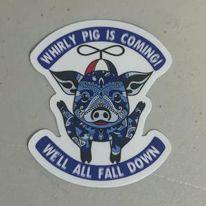May include: A sticker featuring a blue pig with intricate patterns and a red hat. The text "WHIRLY PIG IS COMING!" arches above the pig, while "WE'LL ALL FALL DOWN" curves below.