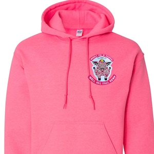 May include: A bright pink hooded sweatshirt with a front pocket and drawstring hood. The sweatshirt features a graphic of a pig with the text "WHINEY PIG IS COMING! WELL ALL FALL DOWN" on the upper left chest. The sweatshirt is made of a soft material.