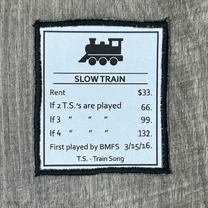 May include: A white rectangular patch with a black border and the words "SLOW TRAIN" and a train graphic. The patch includes text about rent and the phrase "First played by BMFS 3/15/16."