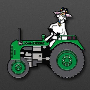 May include: A green John Deere tractor with a white goat wearing a rainbow necklace driving it. The goat has a pink nose and colorful eyes.