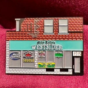 Puede incluir: Un pin de metal que representa una tienda con un toldo verde que dice "Mike Kelly's Westside". La tienda tiene una fachada de ladrillo y ventanas con varios logotipos, incluidos Bud Light, Budweiser Select y una bicicleta. La puerta tiene el n&uacute;mero "1515" en ella.