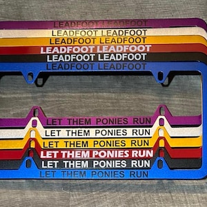 May include: A set of six license plate frames in various colors, including purple, white, yellow, red, black, and blue. Each frame features the text "LEADFOOT LEADFOOT" at the top and "LET THEM PONIES RUN" at the bottom.