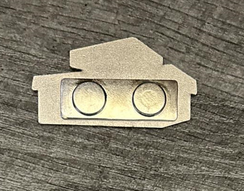 May include: A silver metal name tag shaped like a house with two round magnets on the front.