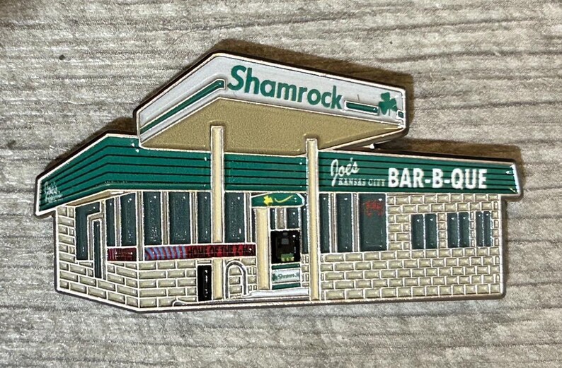 May include: A green and white enamel pin depicting a vintage gas station with the text "Shamrock" and "Joe's Kansas City BAR-B-QUE" on the front.