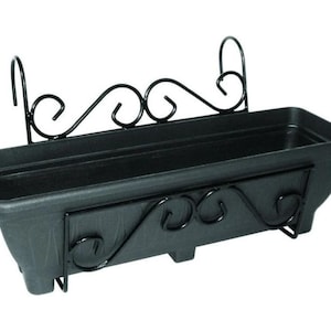 May include: Black plastic planter with a metal frame. The frame has a decorative scroll design. The planter is designed to hang on a wall or railing.