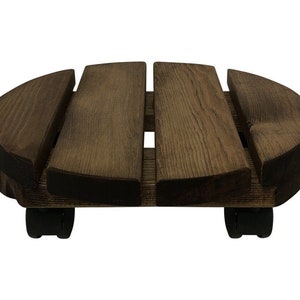 May include: A round wooden plant stand with four wheels. The stand is made of dark brown wood and has a slatted design. The wheels are black and are located on the bottom of the stand.