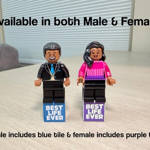 May include: Two LEGO minifigures standing on rectangular tiles. The left figure wears a black suit with a blue tie, standing on a blue tile reading BEST LIFE EVER. The right figure wears a pink and purple top, standing on a purple tile reading BEST LIFE EVER.