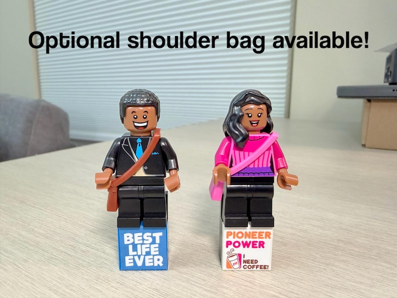 May include: Two plastic minifigures standing on rectangular blocks. The left figure wears a black suit with a blue tie and a brown shoulder bag. The right figure wears a pink top and a pink shoulder bag. Text reads: Optional shoulder bag available!