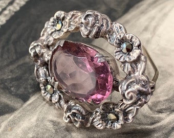 Silver Victorian brooch features a dainty yet weighty design showcasing a captivating light paste amethyst-colored stone at its center