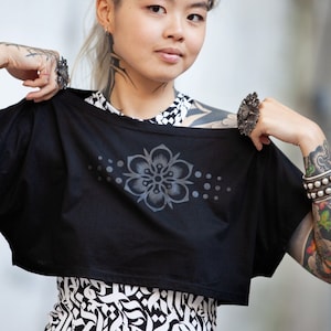 May include: A black cropped t-shirt with a gray floral design and a row of gray dots. The shirt is made of a soft, comfortable fabric and has a relaxed fit.