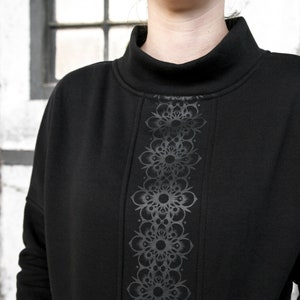 May include: Black mock neck sweatshirt with a vertical design of repeating black floral patterns.